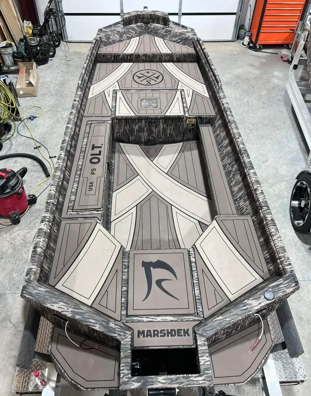 Top-down view of a custom gray camo metal boat hull in a workshop, with open deck panels and “MARSHAWK” label.