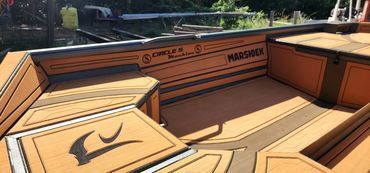 Wooden boat deck with bench seating and a black wave logo on tan panels by the water