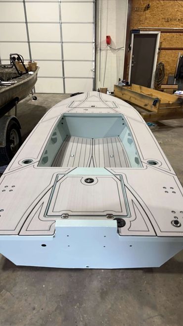 White boat hull in a workshop, seen from above with blue trim and unfinished deck details.