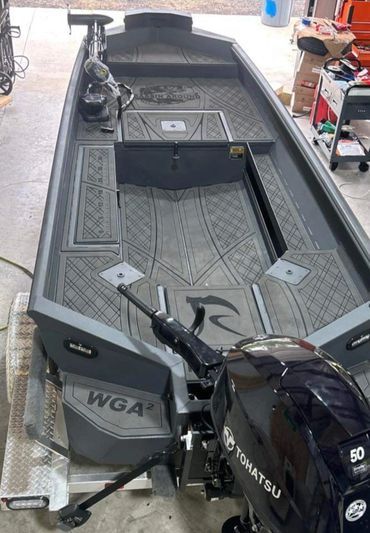 Gray fishing boat on a trailer in a garage, viewed from above, with a Suzuki outboard motor at the stern.