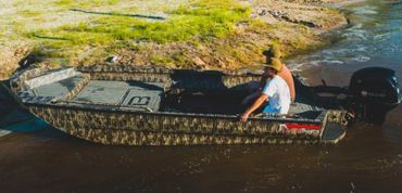 Person in a narrow boat on a muddy river, with gear and a small outboard motor.