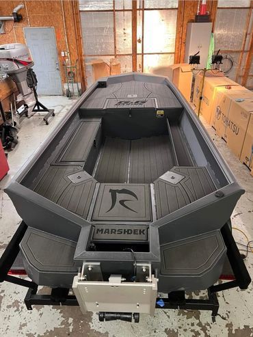 Gray MARSDEK boat in a workshop, centered on a trailer with tools and boxes around it.