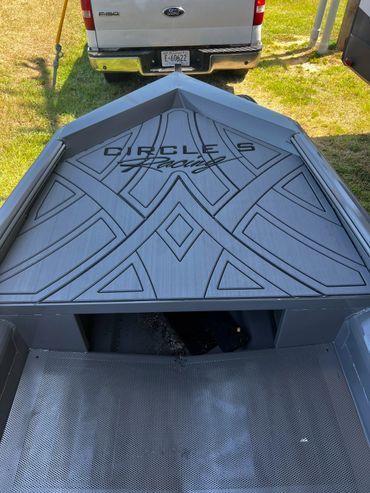 Black geometric-patterned trailer or cargo box with open front, parked on grass behind a white van.