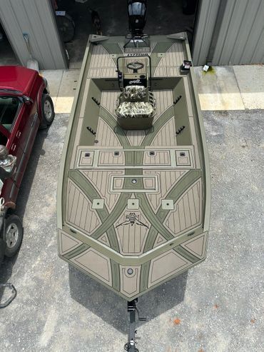 Top-down view of a tan military-style boat docked beside a red car and gray building.