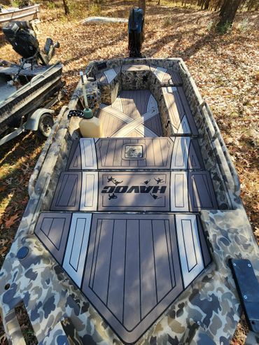 Camouflage boat deck with gray panels and logo, outdoors with fishing gear nearby