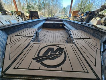 Open boat deck with tan flooring and a large black logo at the center, viewed from the stern