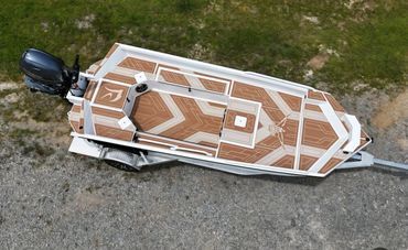 Overhead view of a small motorboat with tan-and-white deck on grass, motor at the stern