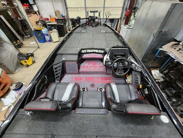 Interior of a black racing boat with black-and-red seats, steering wheel, and dashboard in a workshop