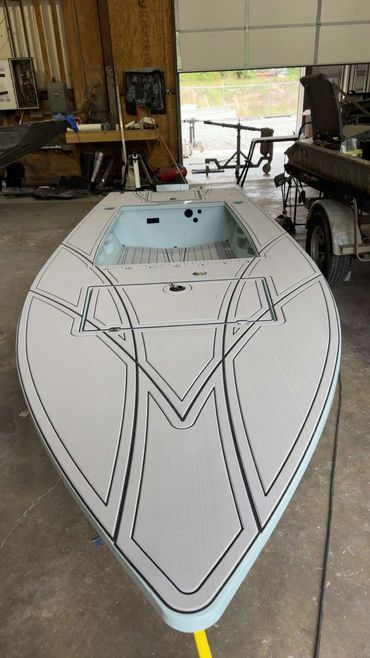 White boat hull in a workshop, front view with black taped deck lines and open top hatch.