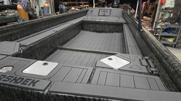 Gray aluminum fishing boat hull on factory floor, with raised deck panels and side rails being assembled