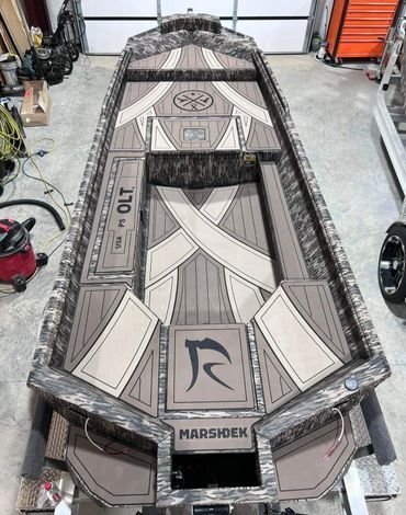 Top-down view of a custom camo-patterned aluminum boat hull in a garage, labeled MarshKing.