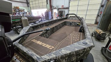 Camouflage-pattern fishing boat in a workshop garage with open hatch and equipment nearby