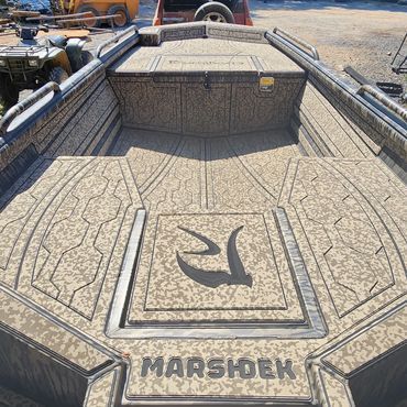 Close-up of a textured gray MarshDek boat deck with logo, viewed from the stern in a yard