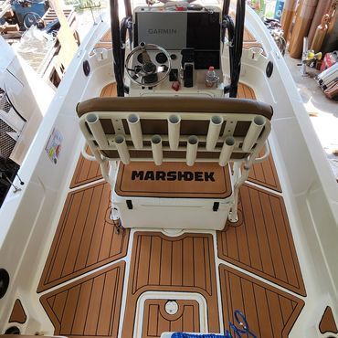 View from helm of a white boat with wood-deck flooring and tan seating, showing MARSHDEK branding.