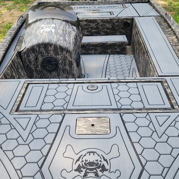 Camouflaged boat deck with hex-pattern panels, a skull graphic, and a large cylindrical tank at left.