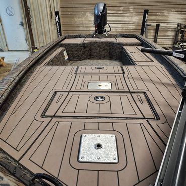 Boat deck with tan non-slip flooring, hatches, and a motor at the stern in a workshop.