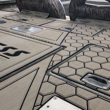 Close-up of a gray boat deck with patterned panels, hatches, and seating bases