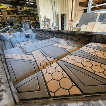 Workshop table covered with geometric tiled panels in gray and tan, with shelves and tools in the background