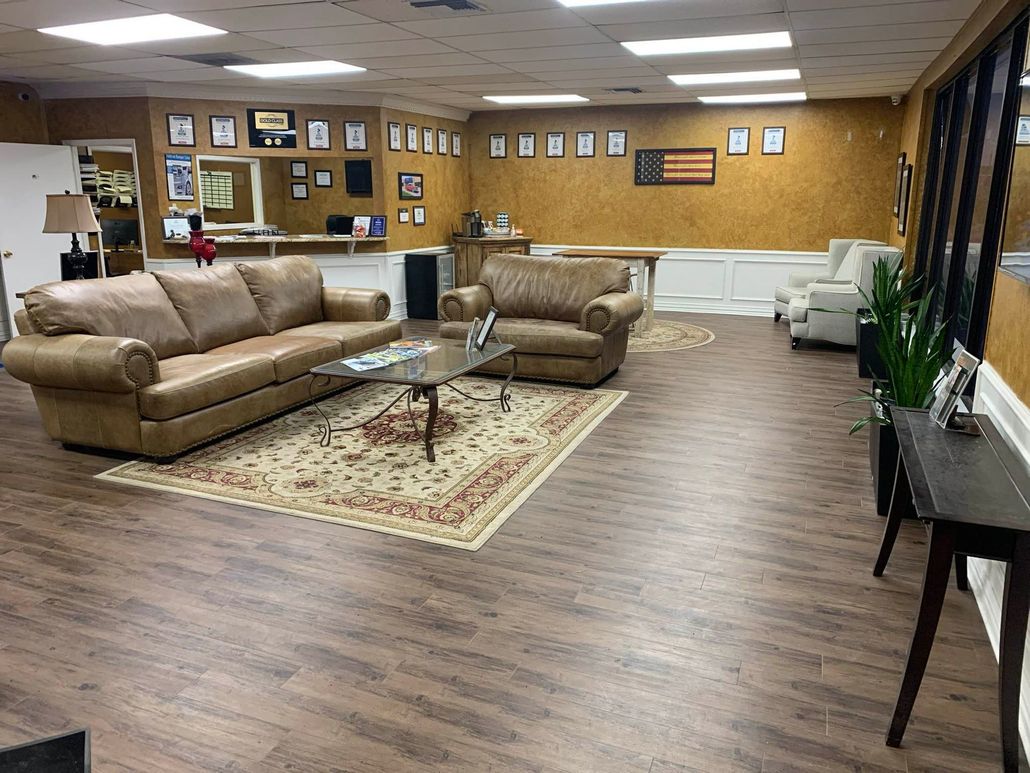 Spacious lounge with tan leather sofas, coffee table, rug, wood floors, and wall decor under fluorescent lights