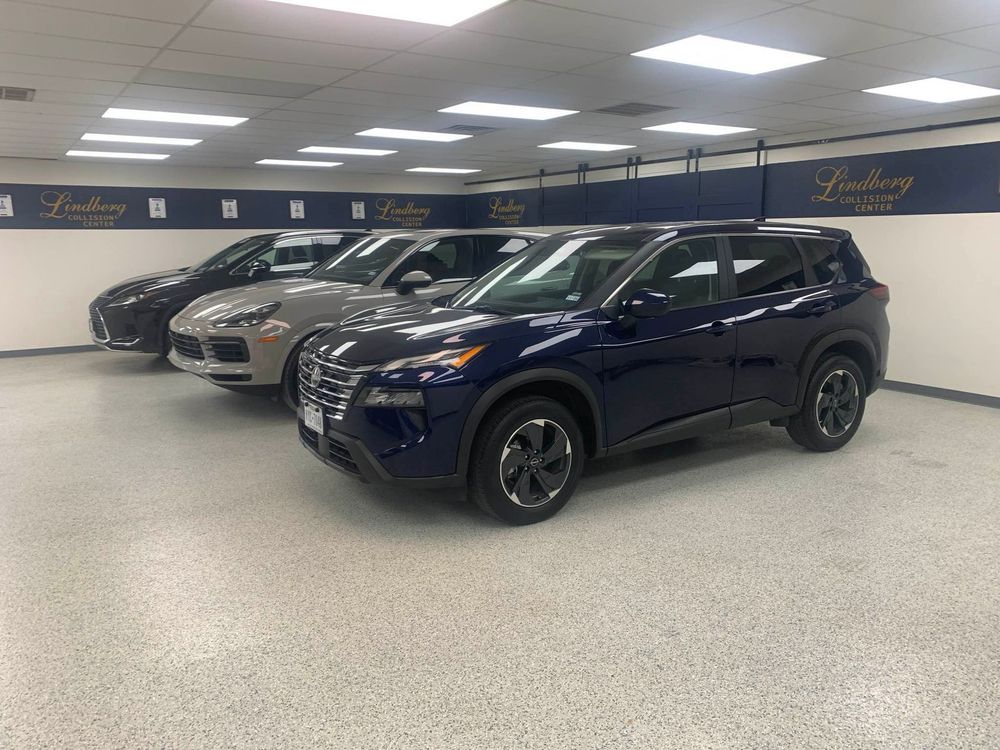 Row of SUVs in a dealership showroom: dark blue, gray, and black. Bright lights and logo on wall.