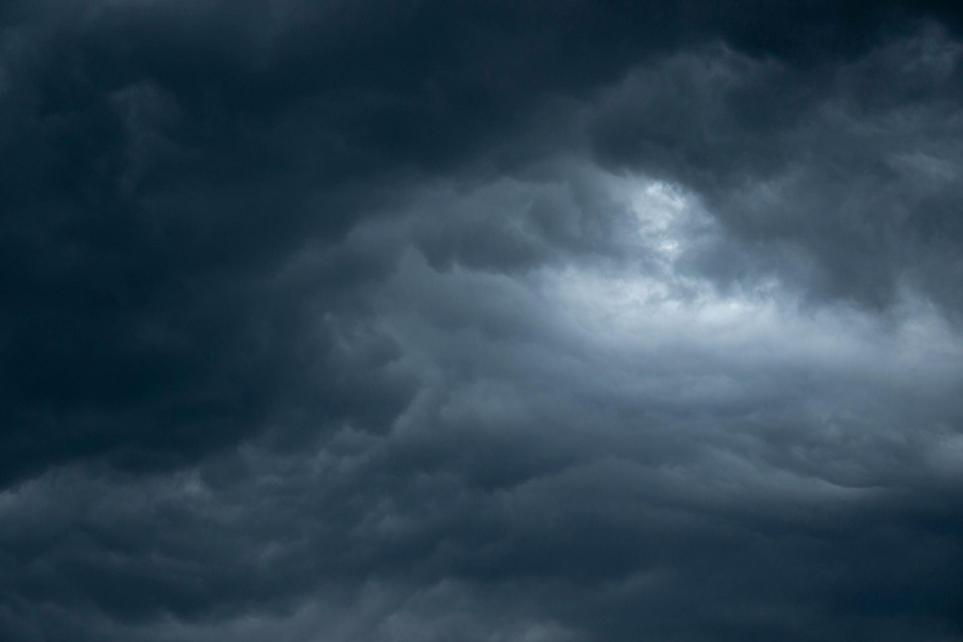 Dark, dense, and turbulent storm clouds fill the sky, with a small patch of brighter light glowing near the center.