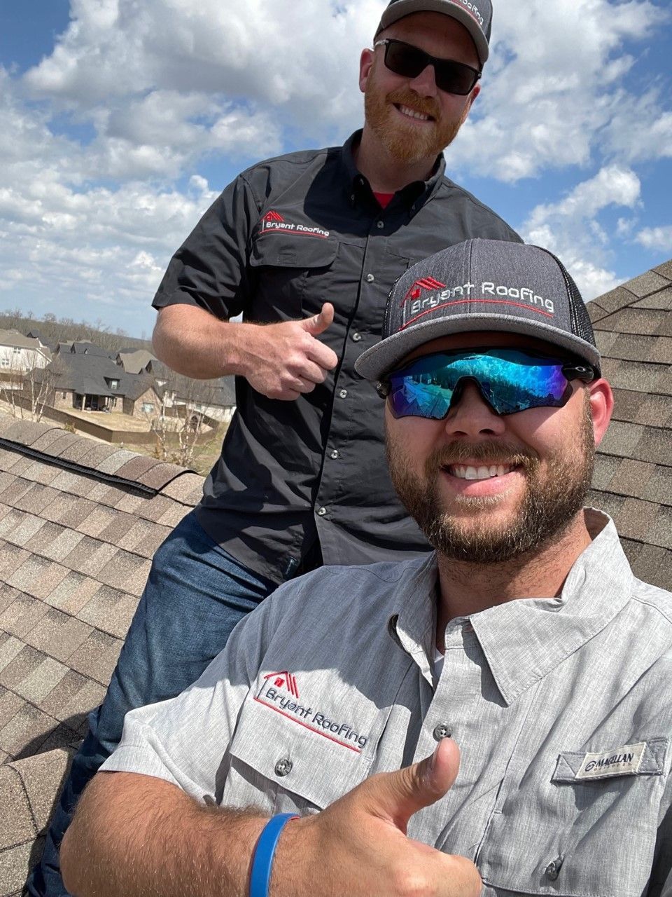 Two men are sitting on top of a roof giving a thumbs up.