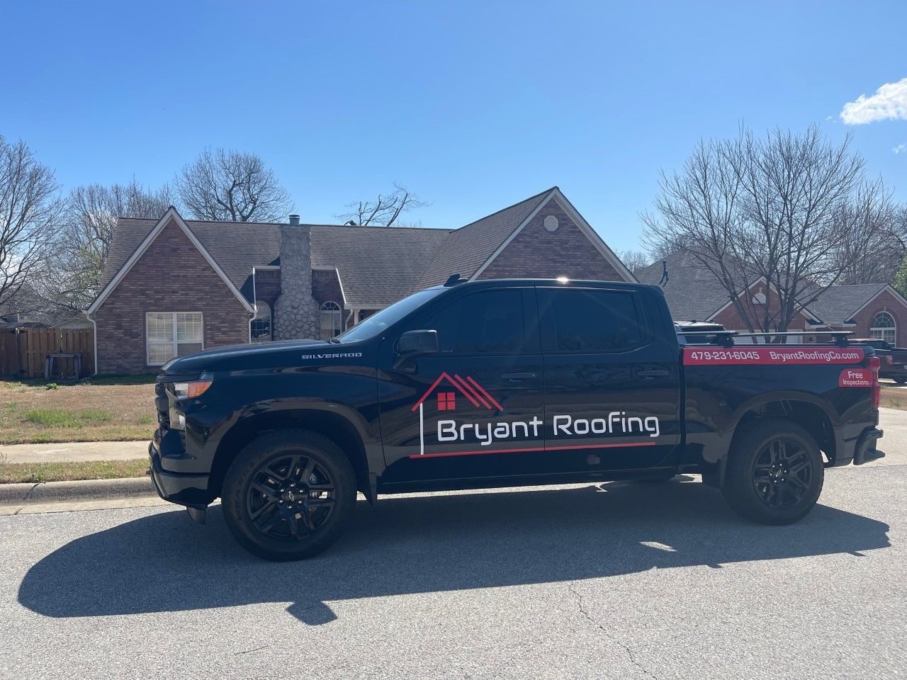 A black truck with the word bryant roofing on it is parked in front of a house.