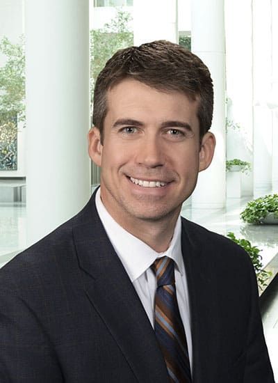 Smiling man in a dark suit and striped tie standing in a bright office setting