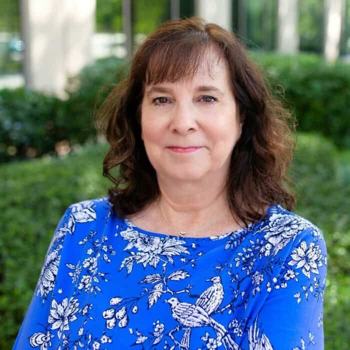 Woman in a blue floral top posing outdoors with a slight smile