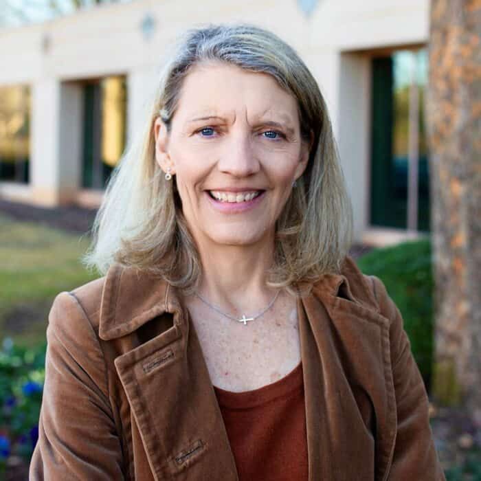 Smiling woman in a brown jacket standing outdoors near a building