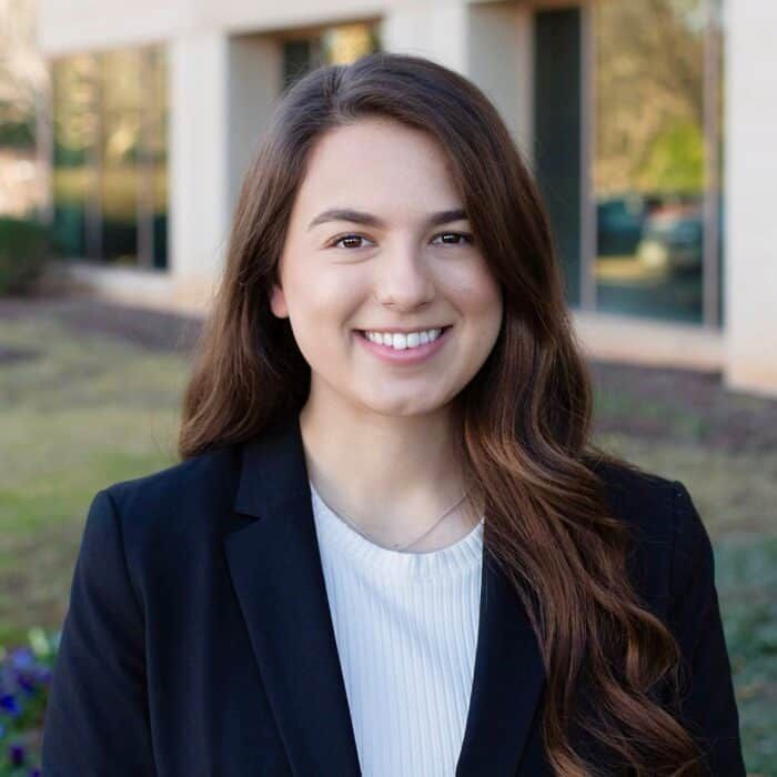 Smiling woman in a dark blazer standing outdoors in front of a building