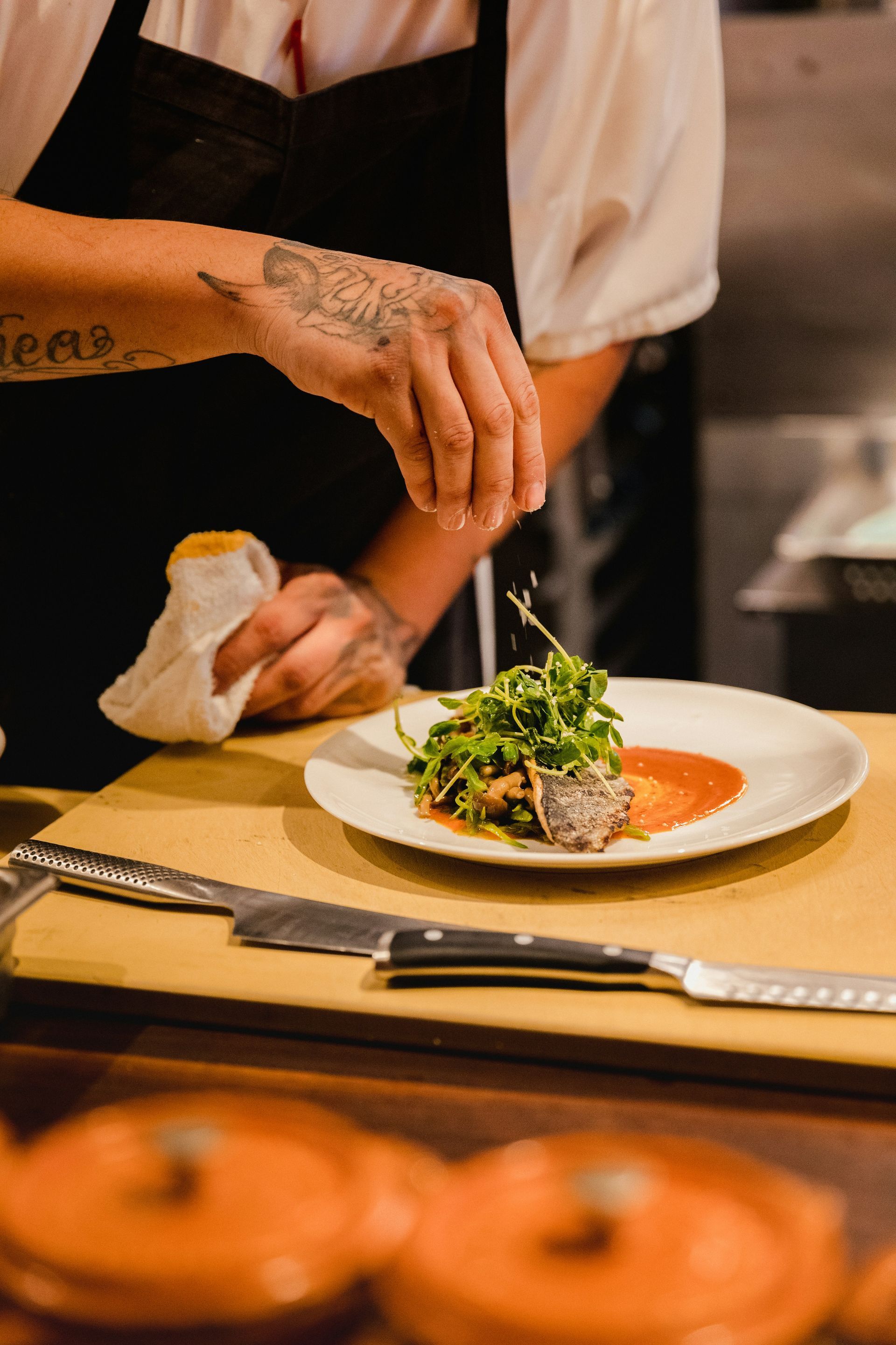 Chef plating a gourmet dish on a white plate in a restaurant kitchen