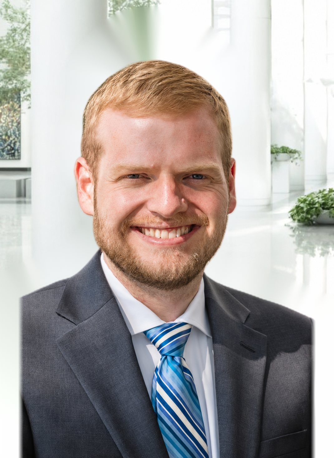 Smiling man in a gray suit and blue striped tie against a bright office backdrop