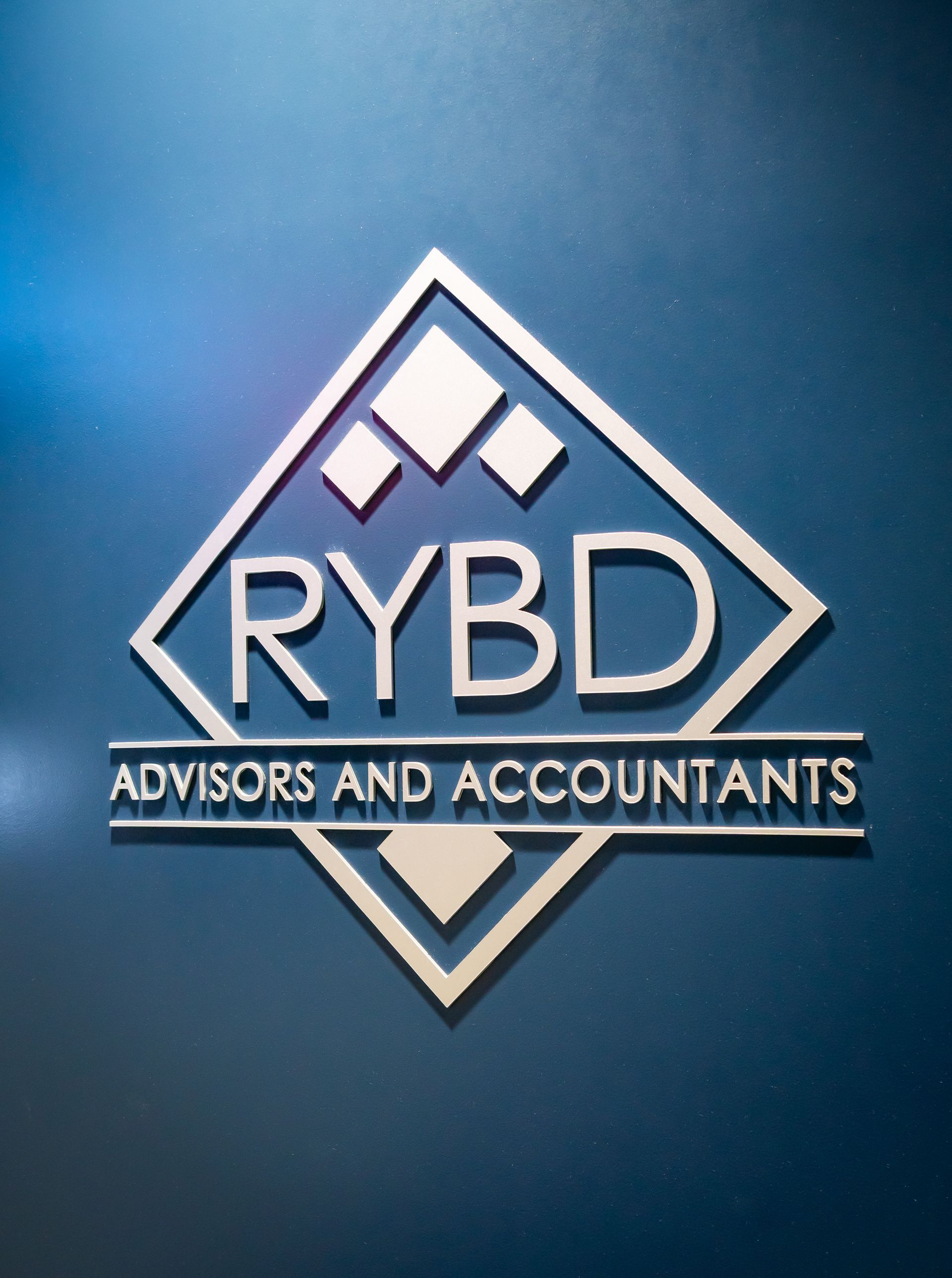 RYBD Advisors and Accountants logo on a blue wall, with a diamond outline and metallic lettering