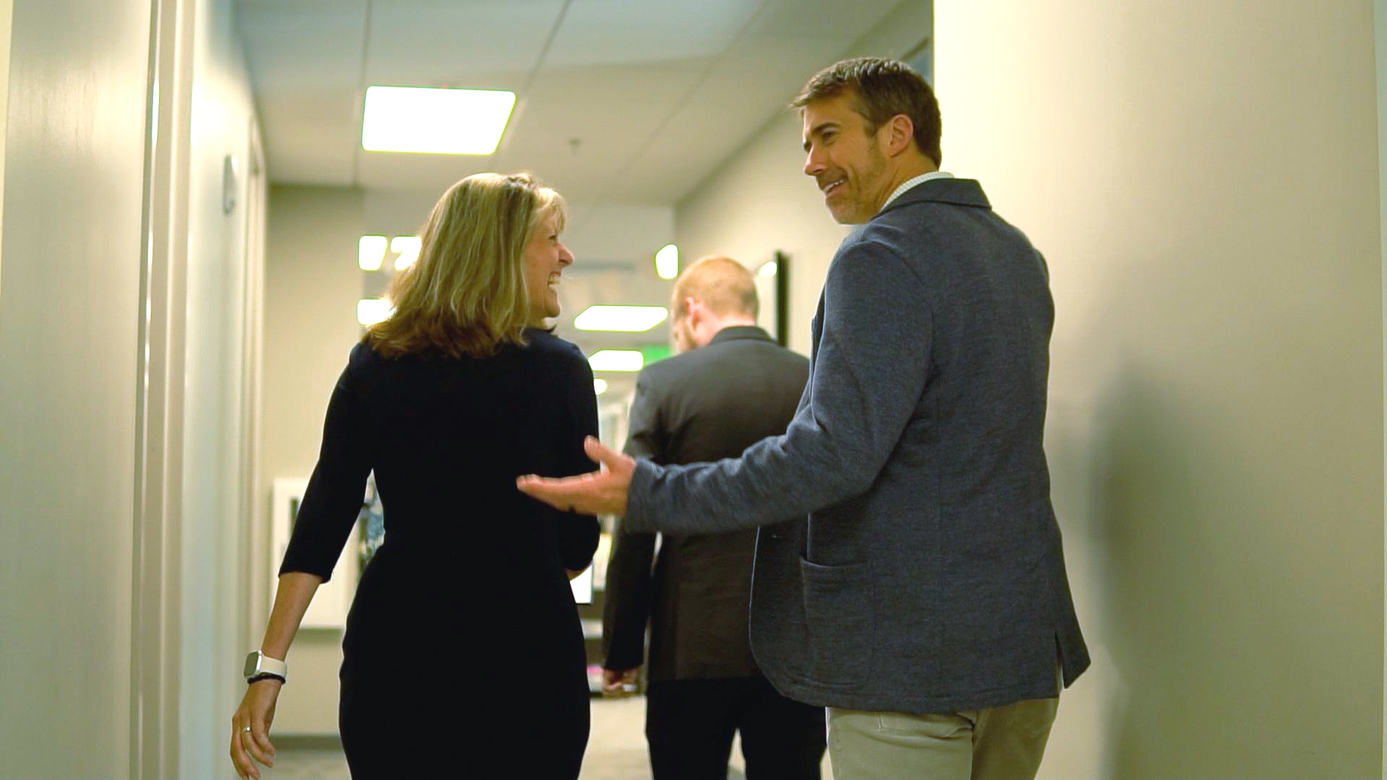 Three people walking down a narrow hallway, with one person gesturing while talking.