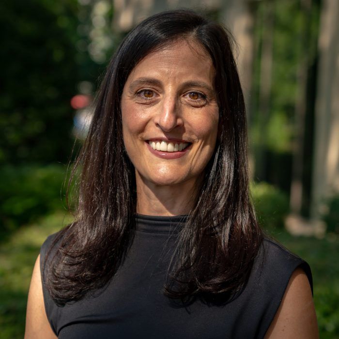 Smiling woman in a black sleeveless top standing outdoors among green trees