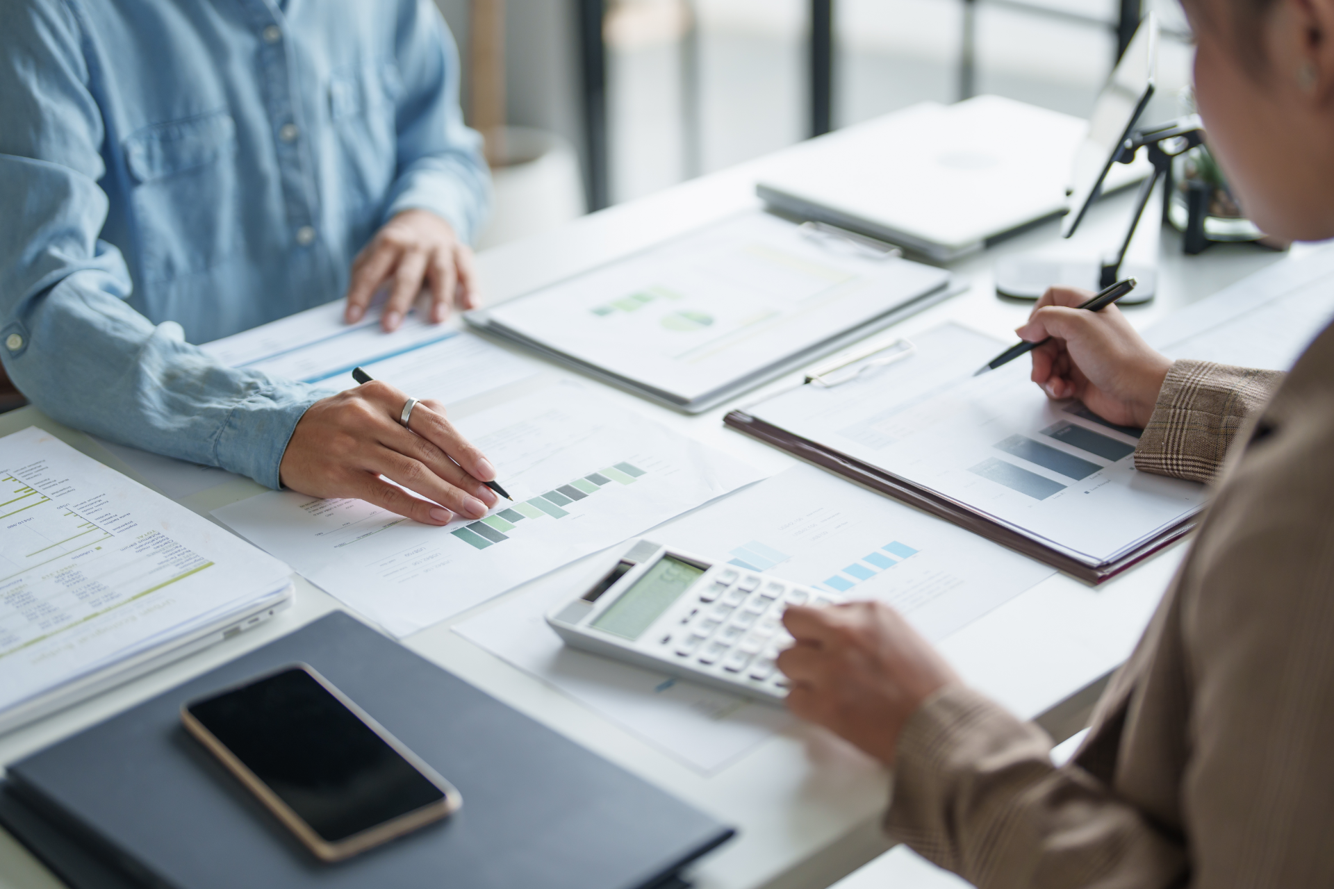 People reviewing financial charts and documents at a desk with a calculator and smartphone