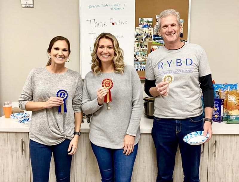 Three smiling people holding award ribbons in an office break room