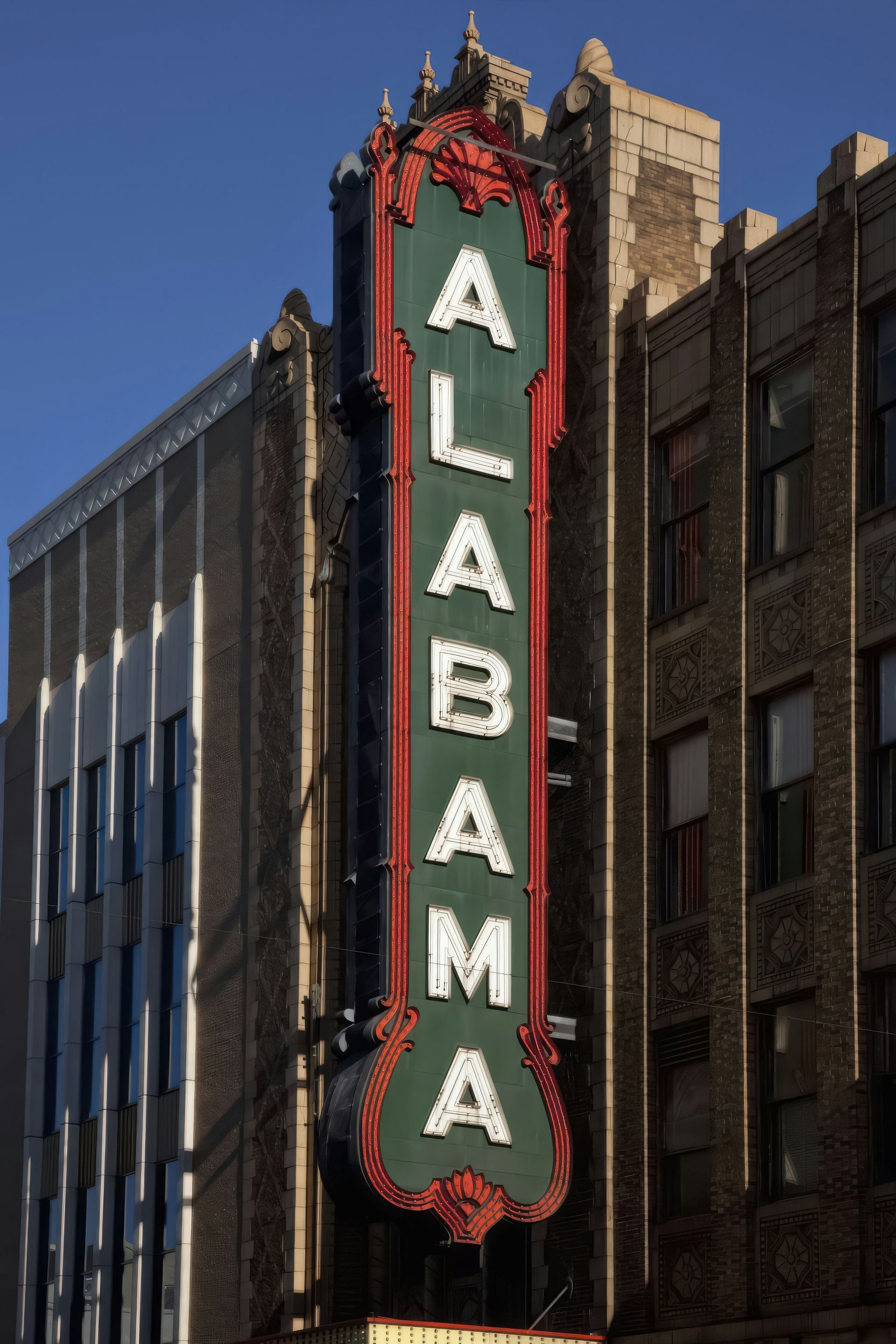 Vertical Alabama theater sign with red trim on a brick building against a blue sky
