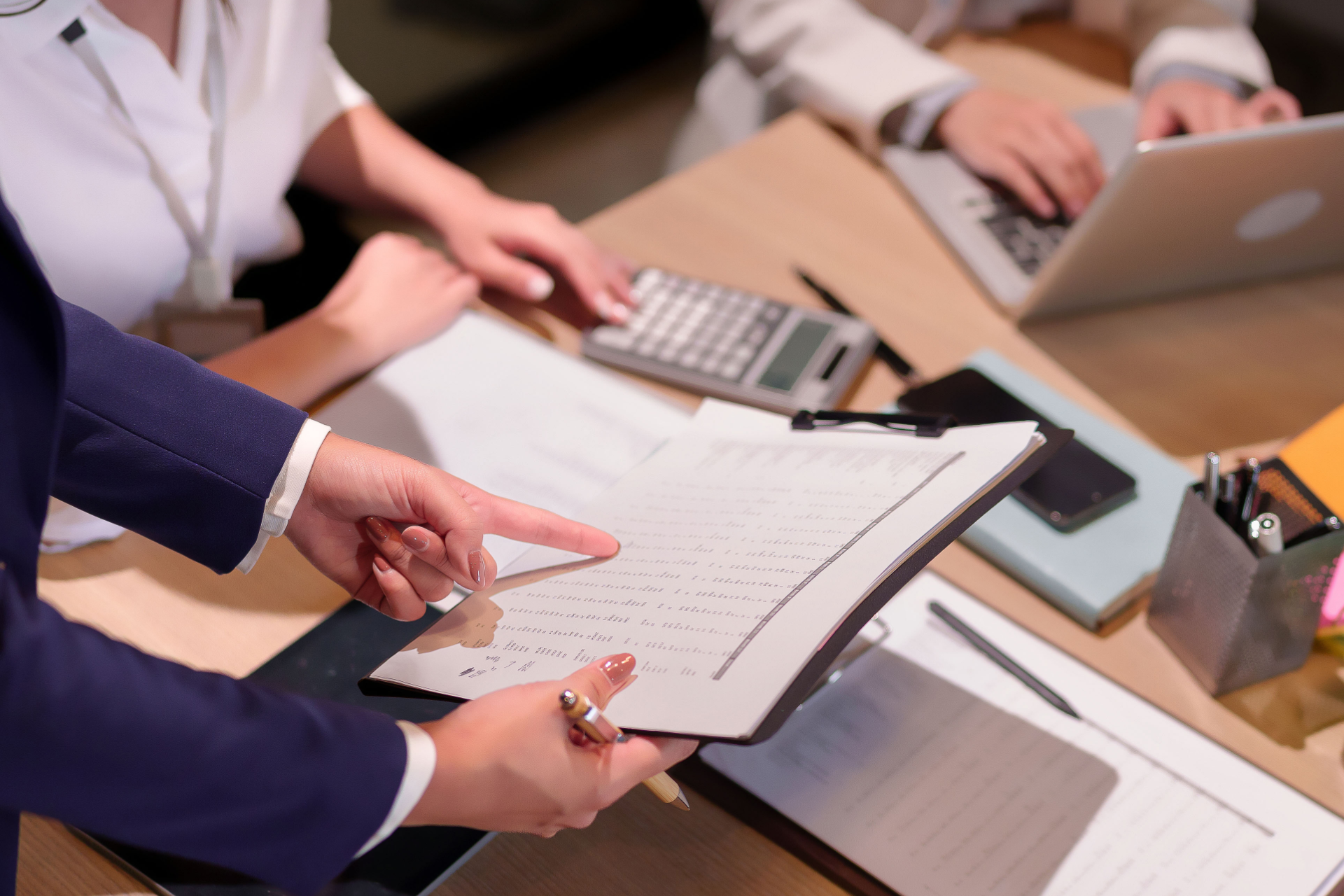 Hands pointing at a notebook during a business meeting with a calculator, laptop, and papers on the table