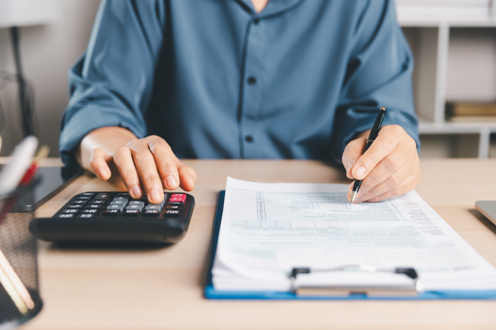 Person using calculator and writing on paperwork at a desk