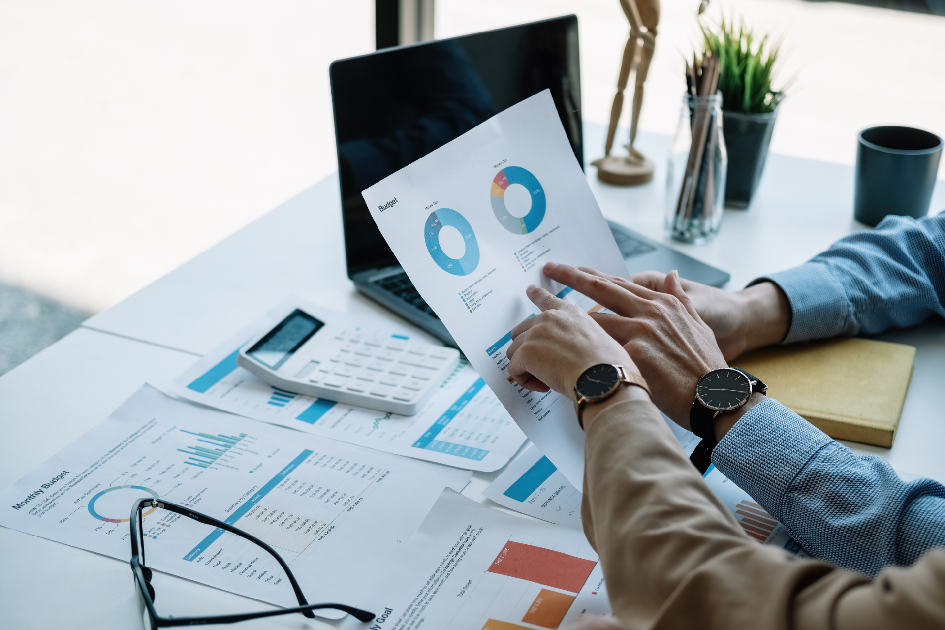 Hands reviewing charts and graphs on a desk beside a laptop in a bright office