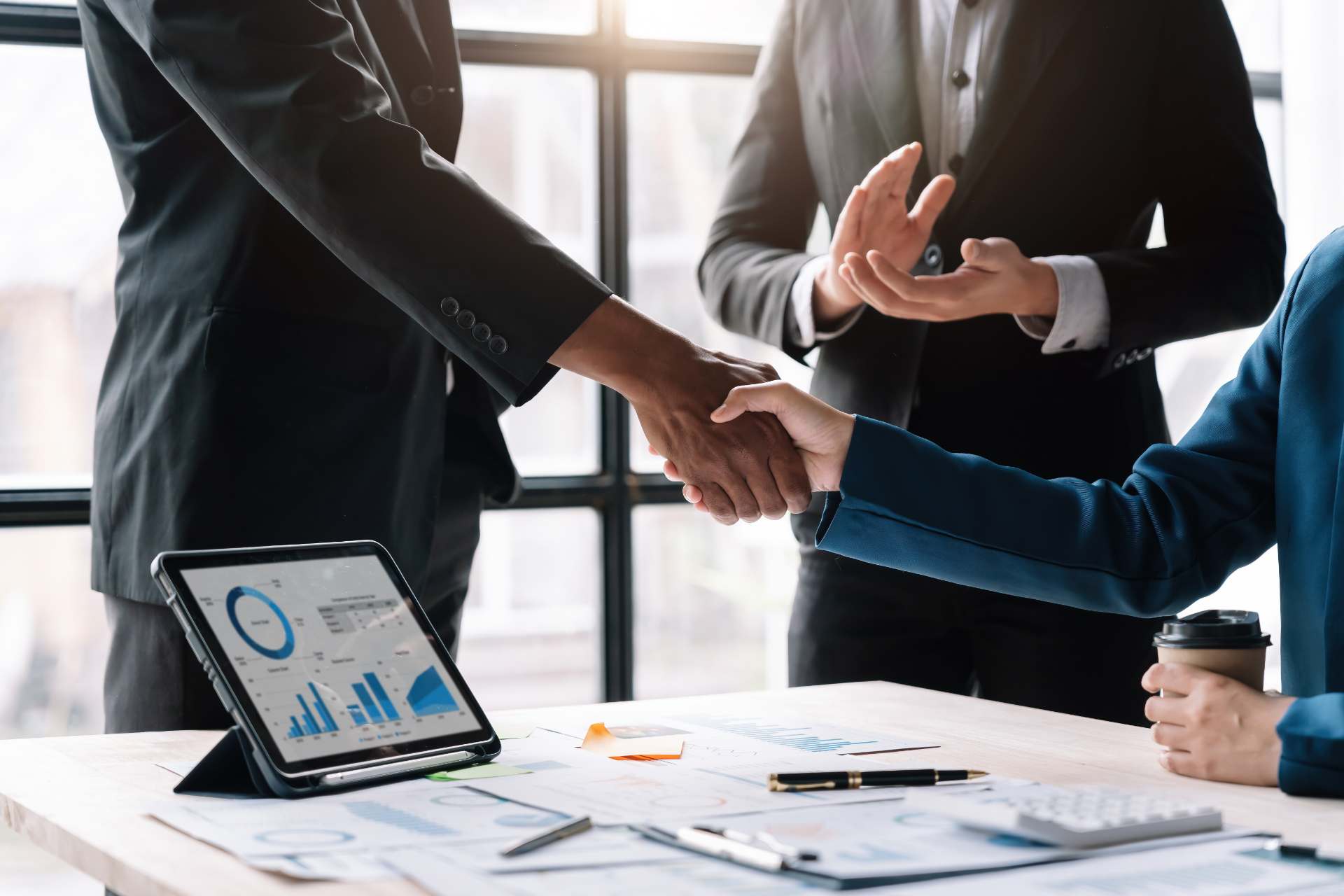 Business meeting with people shaking hands over a laptop displaying charts and graphs