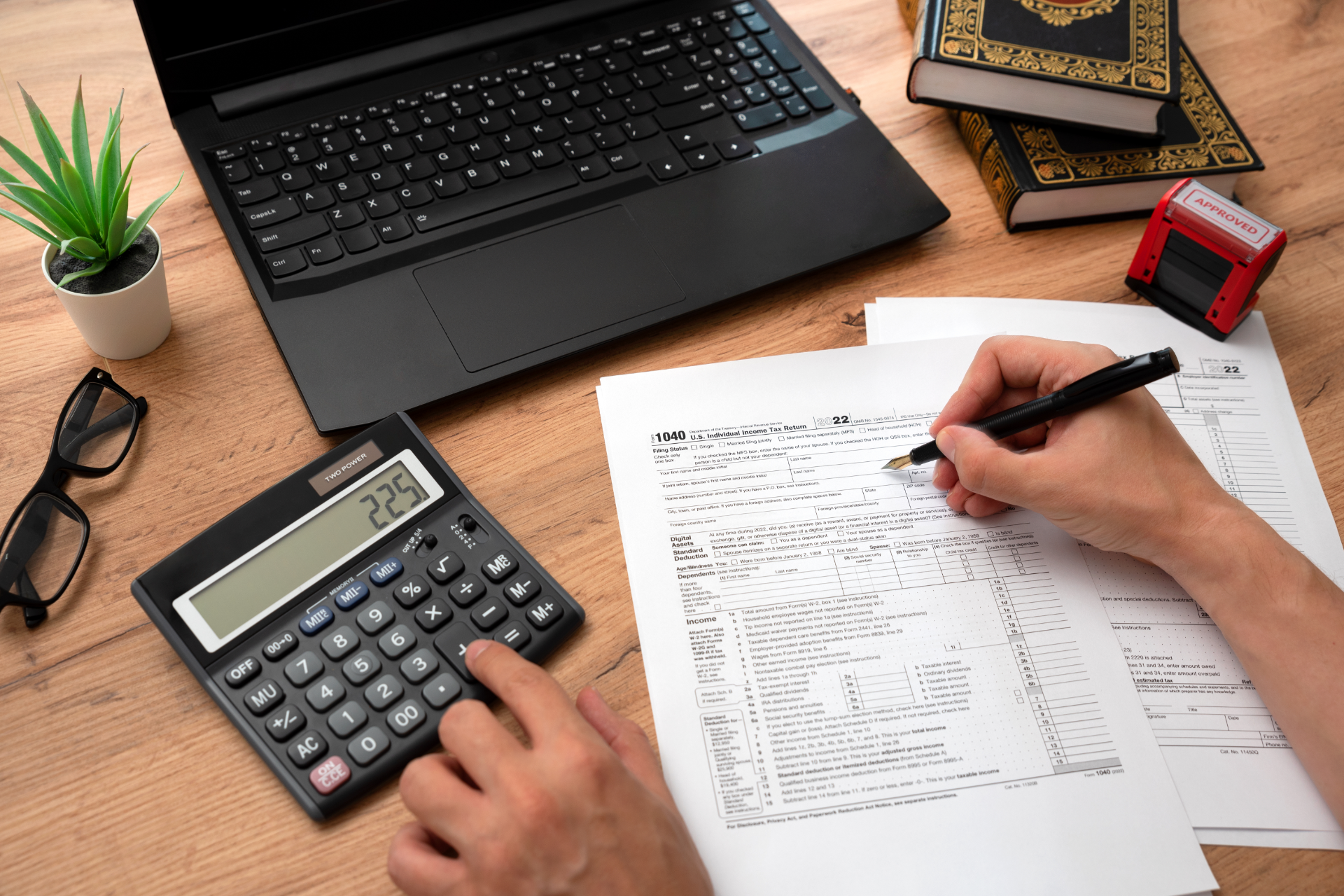 Hands calculating with calculator and writing on paperwork beside a laptop on a desk