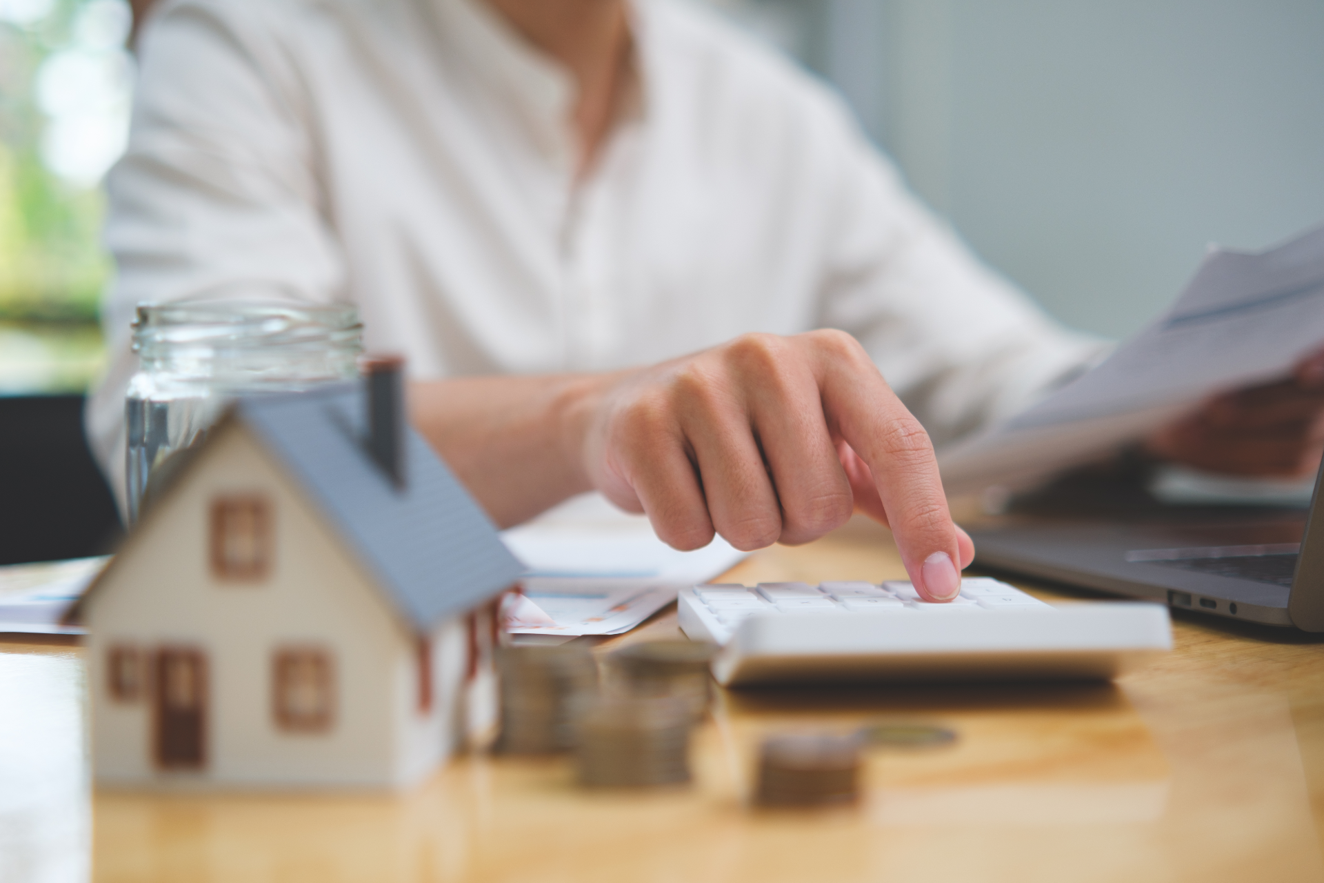 Person reviewing documents beside a small house model and calculator on a desk