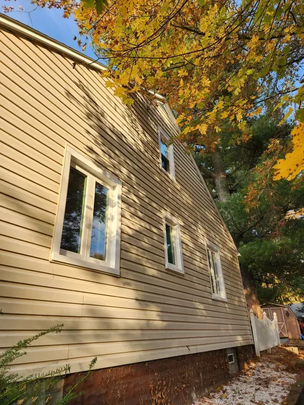 Beige house exterior with white-trimmed windows and autumn trees overhead.