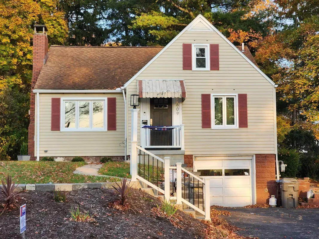 White house with red shutters, front porch, and garage on a tree-lined autumn street.