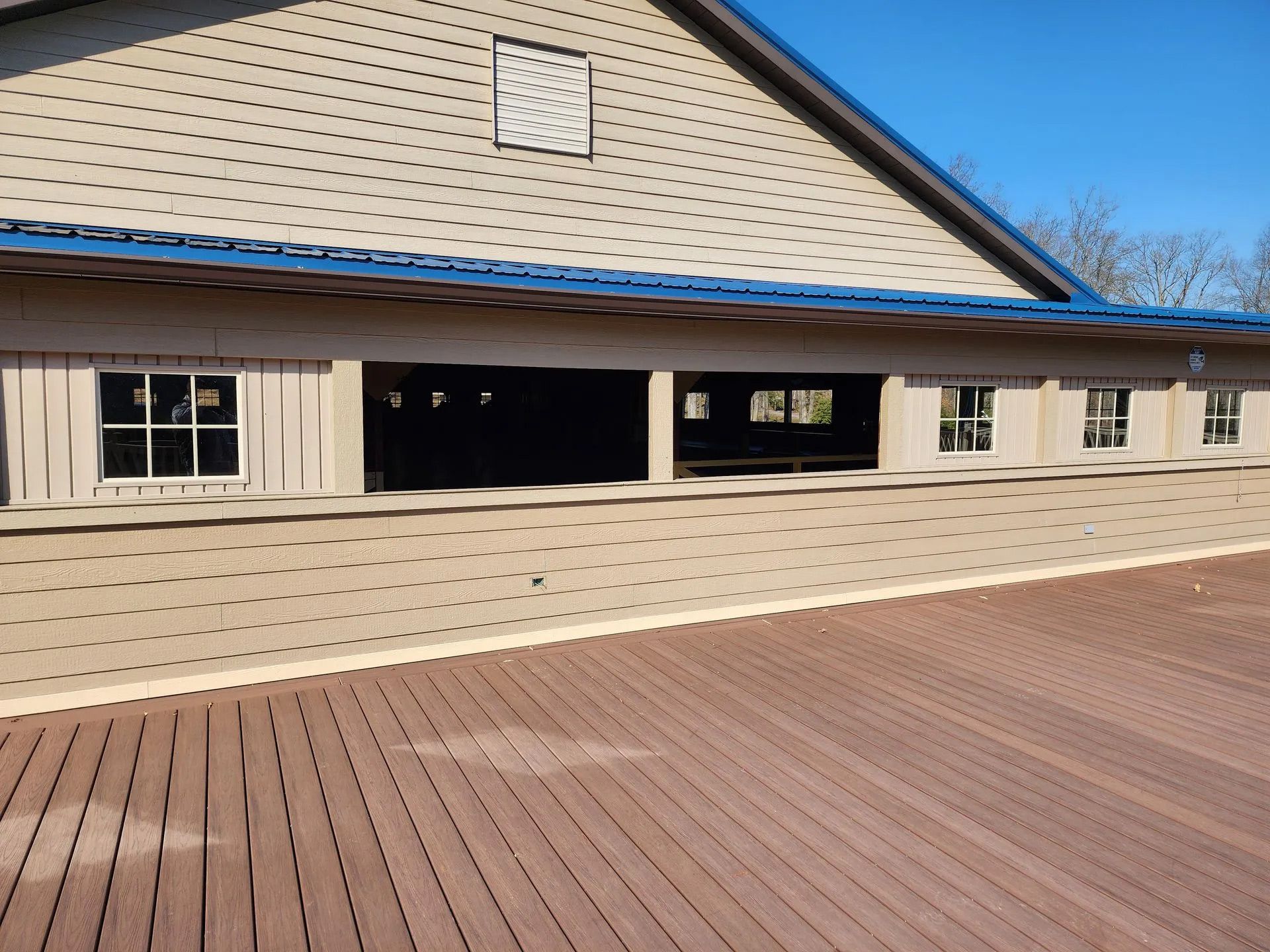 Empty pavilion with beige siding, blue roof trim, and a wooden deck under clear sky