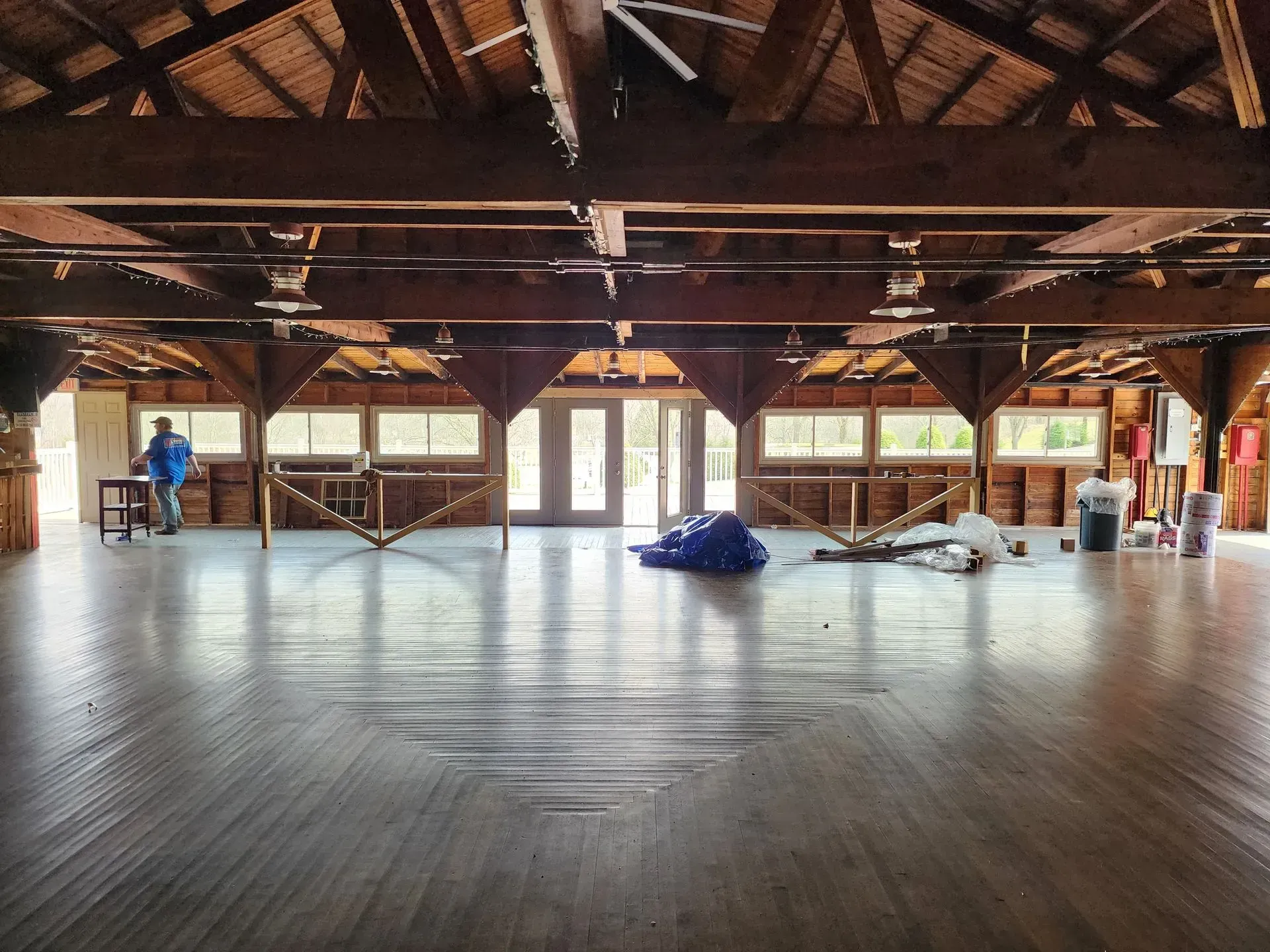Empty wooden hall with exposed beams, large windows, and a few covered items on the floor