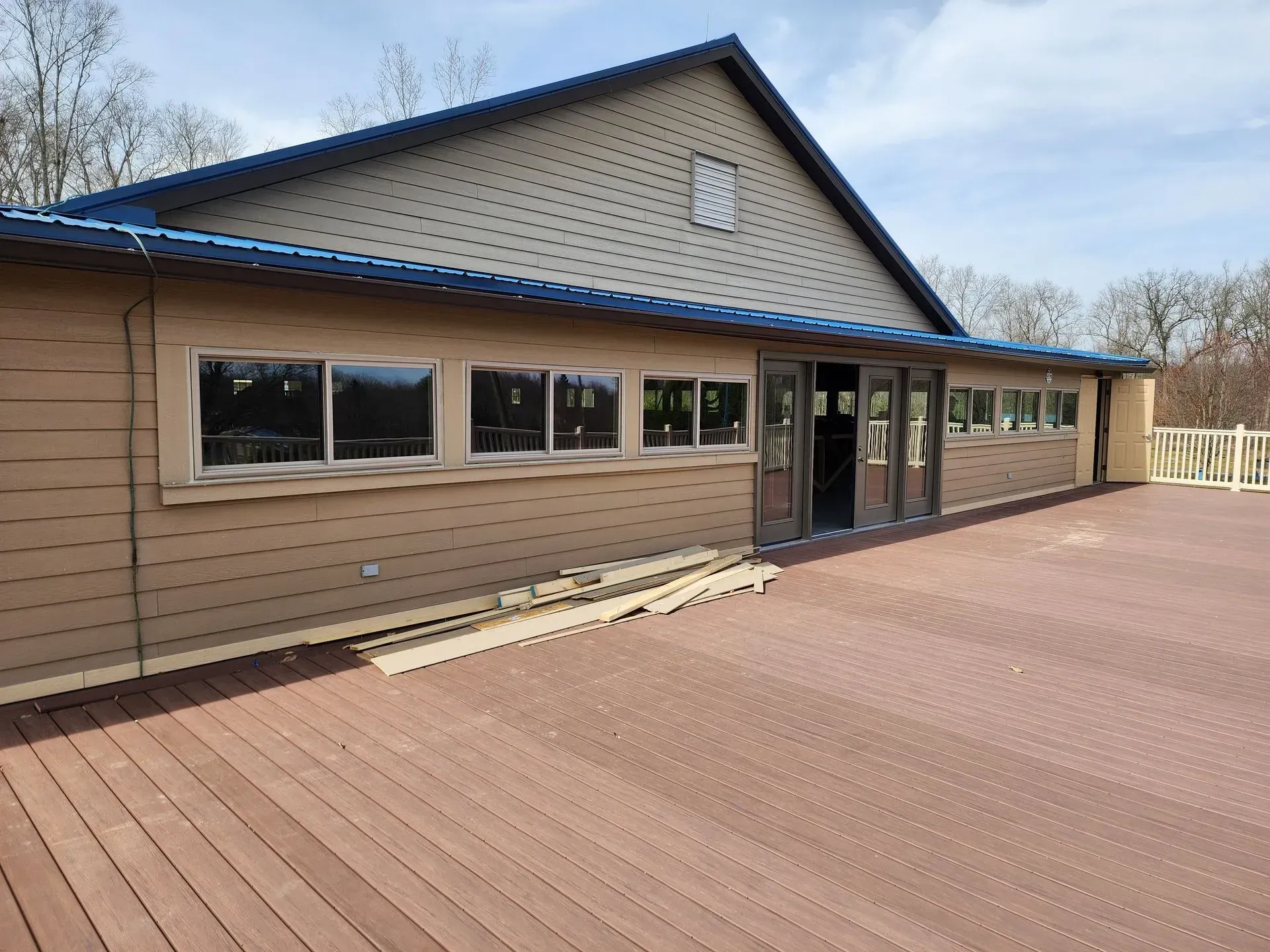Long tan building with blue roof beside a wide wooden deck under a clear sky